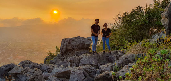 Rear view of people on rock against sky during sunset