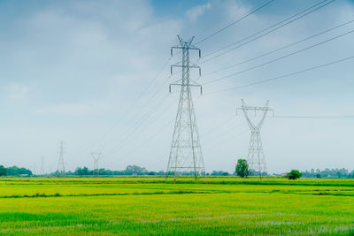 Electricity pylons on field against sky