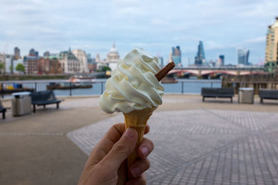 Close-up of hand holding ice cream cone against sky