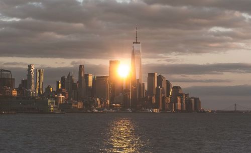 Modern buildings by sea against sky during sunset