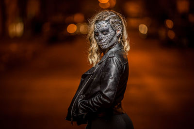 Portrait of woman wearing spooky mask while standing on street at night