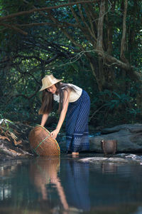 Woman holding basket by pond at forest