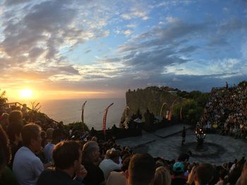 People enjoying at sea against sky during sunset