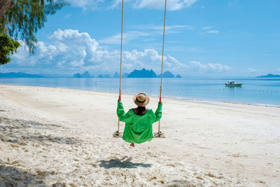 Rear view of woman sitting on swing at beach