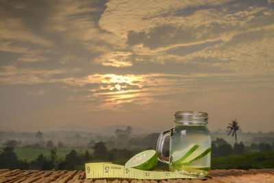 Glass of jar on table against sky during sunset