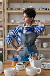 Young creative artisan crafts woman wearing apron looking at the window and thinking