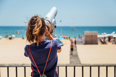 Rear view of woman looking through coin operated binoculars at beach
