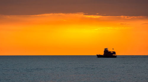 Silhouette boat sailing on sea against orange sky