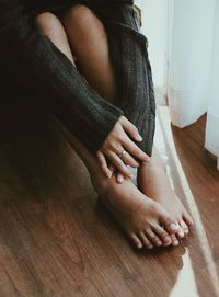 Low section of woman with hands touching feet while sitting on floor at home