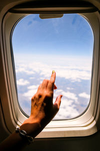 Cropped image of hand against sky seen through airplane window