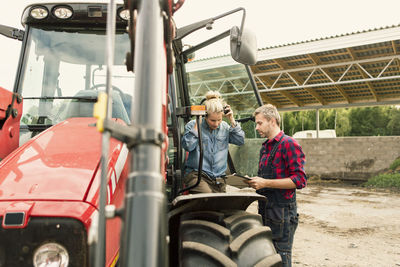 Couple discussing over document by tractor at farm