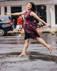 Young woman jumping on wet street in city