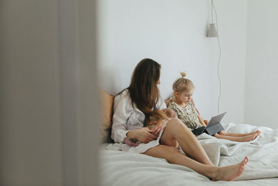 Rear view of woman using laptop on bed at home