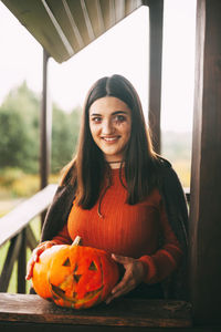 A beautiful girl with dark hair with makeup for the celebration of halloween holds a pumpkin 