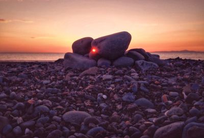 Pebbles on beach against sky during sunset