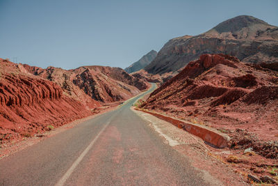 Road leading towards mountains against clear sky