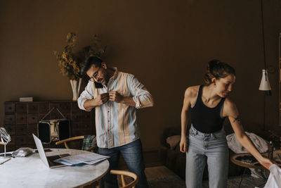 Man buttoning shirt while standing with non-binary person at home