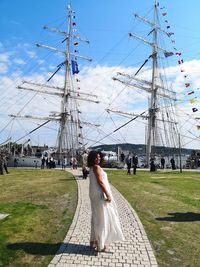 Woman standing on footpath against ships moored at harbor