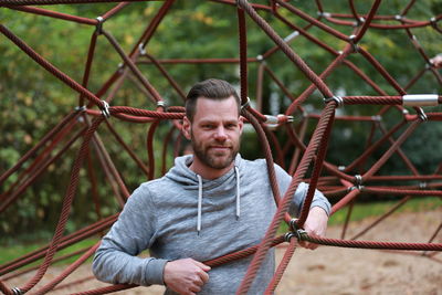 Portrait of man standing amidst jungle gym at playground