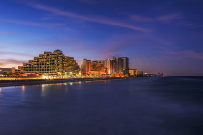 Illuminated buildings by sea against sky at night