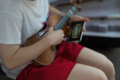 Midsection of woman learning violin through mobile phone at home