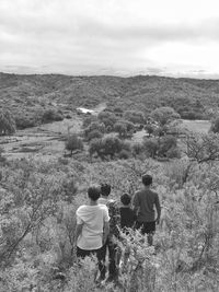 Rear view of people walking on farm against sky