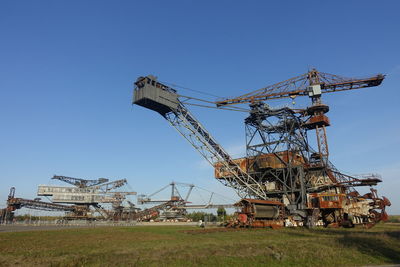 Low angle view of crane on field against clear blue sky