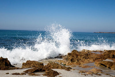 Waves splashing on rocks at shore against sky