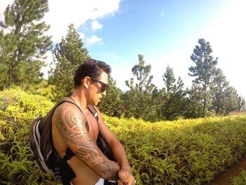 Shirtless tattooed man by plants on field