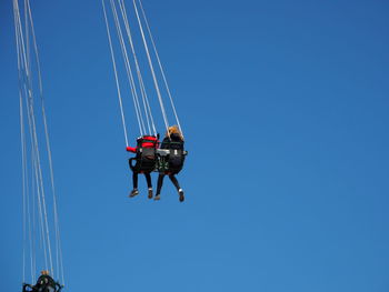 Low angle view of people enjoying in chain swing ride against clear sky