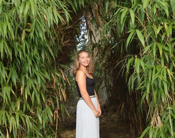 Smiling young woman standing by plants