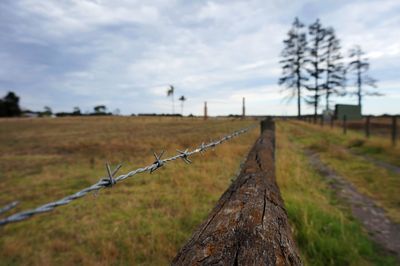 Barbed wire fence on field against sky