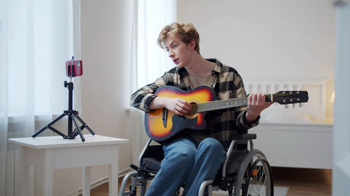 Young man playing guitar while sitting on wheelchair
