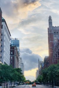 Cars on street by buildings against sky during sunset