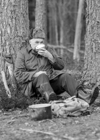 Black and white photo of a forester by the fire, man drinking tea, blurred forest background, wild