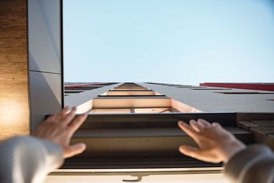 Low angle view of hands raised towards tall building against clear sky