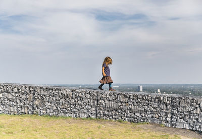 Full length of woman standing on wall against sea