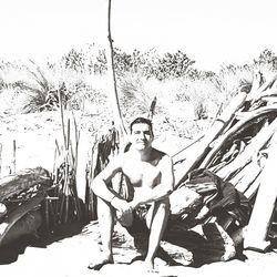 Portrait of young man sitting on plant against sky