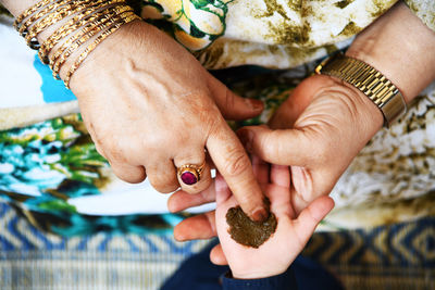 Midsection of woman applying henna tattoo to kids hand