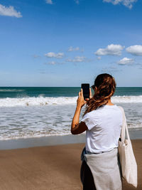 Rear view of woman photographing at beach against sky