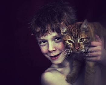 Portrait of boy with cat against black background