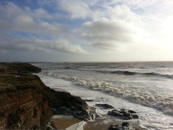 Scenic view of sea by cliffs against cloudy sky