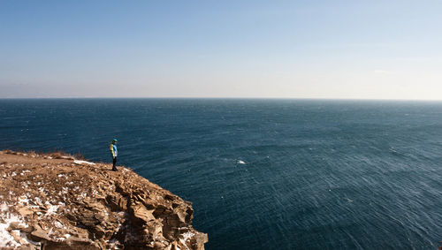 High angle view of man standing on rock formation by sea against sky