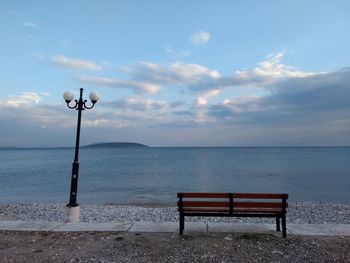 Bench on street by sea against sky