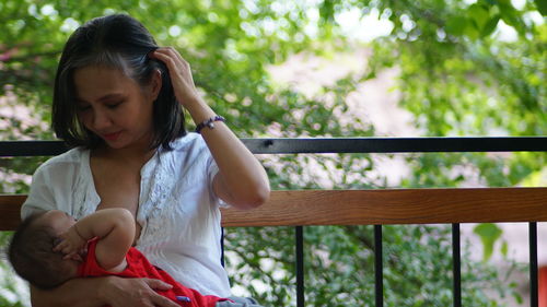 Young woman looking away while sitting on railing