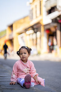 Portrait of cute girl sitting on road in city