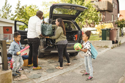 Siblings playing while parents loading luggage in car trunk on driveway