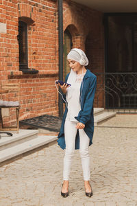 Full length of man using mobile phone standing against brick wall