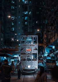 People walking on illuminated street amidst buildings in city at night