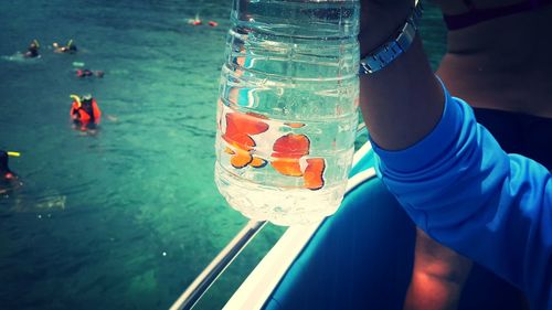 Close-up of cropped hand holding jar with clownfish on boat in sea